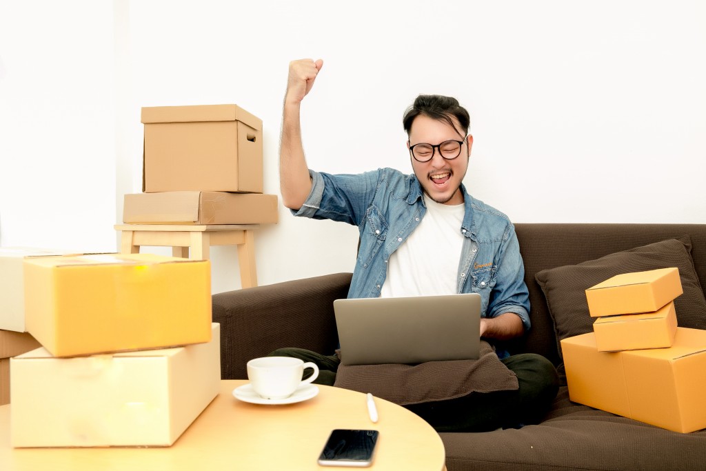 Man rejoicing while looking at his laptop and and being surrounded with boxes