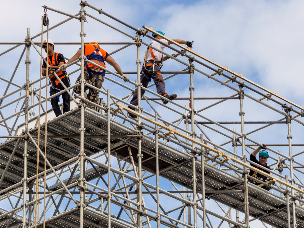 Foreign-born construction workers setting up a scaffold for a building.