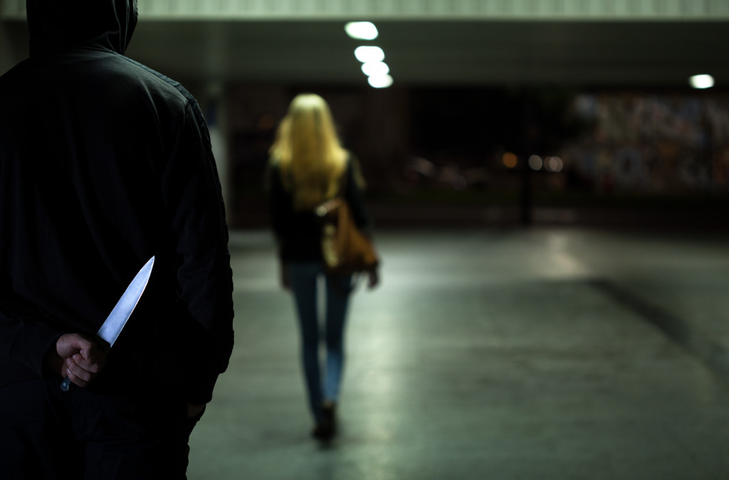 A person in a hoodie holding a knife while following a woman at night