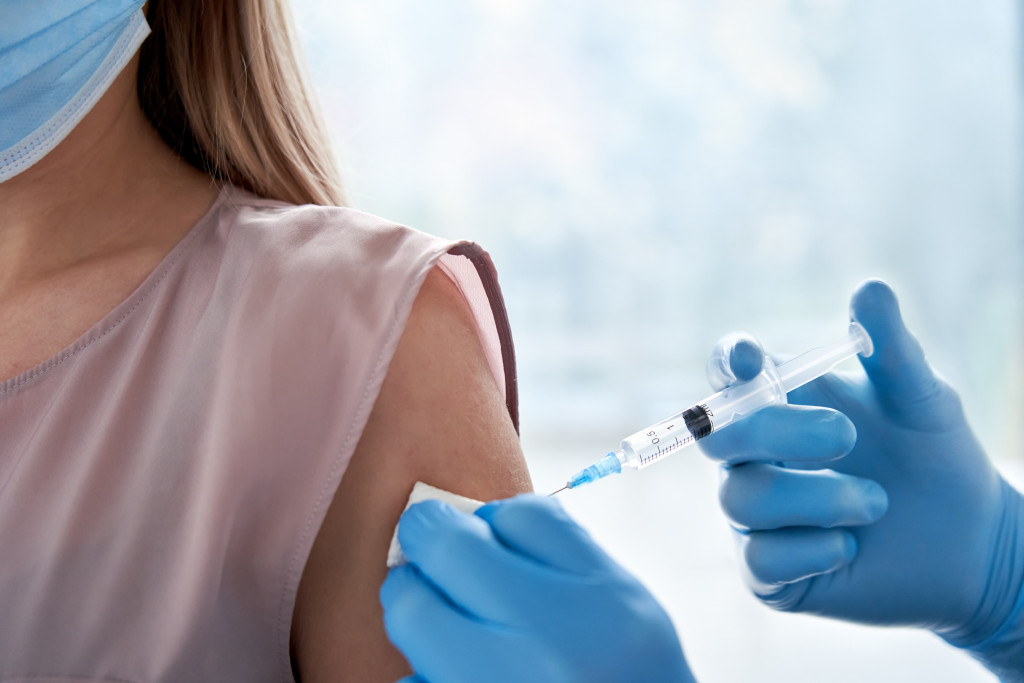 A gloved hand injecting the COVID-19 vaccine on the shoulder of a woman