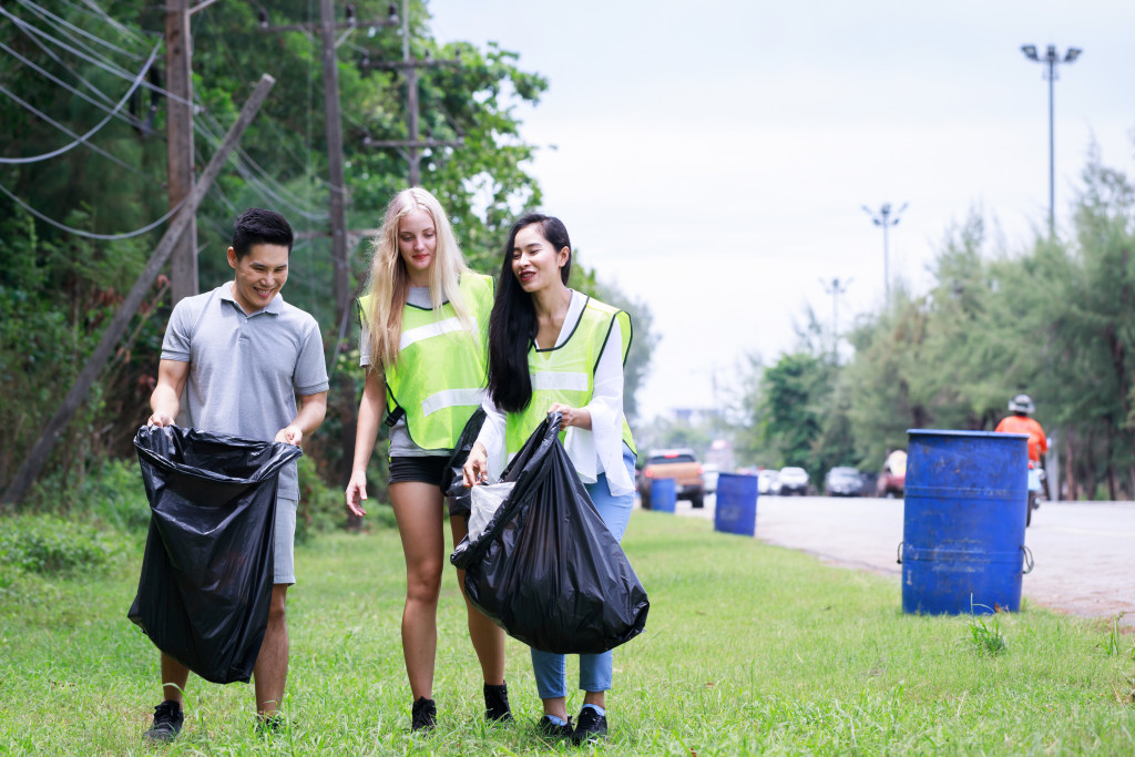 Three employees picking up trash beside a road,