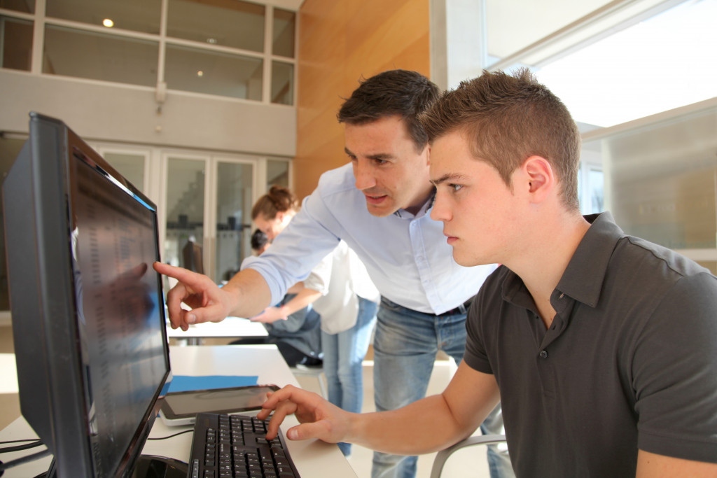 male teacher teaching male student how to use the computer