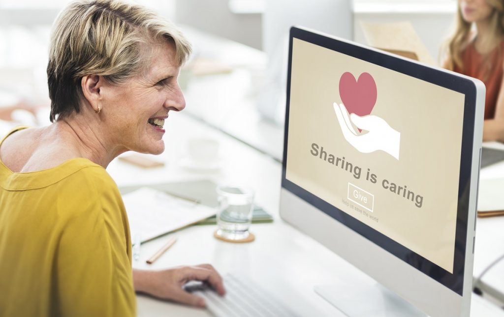 woman smiling while looking at a monitor with the phrase 'sharing is caring' on the screen