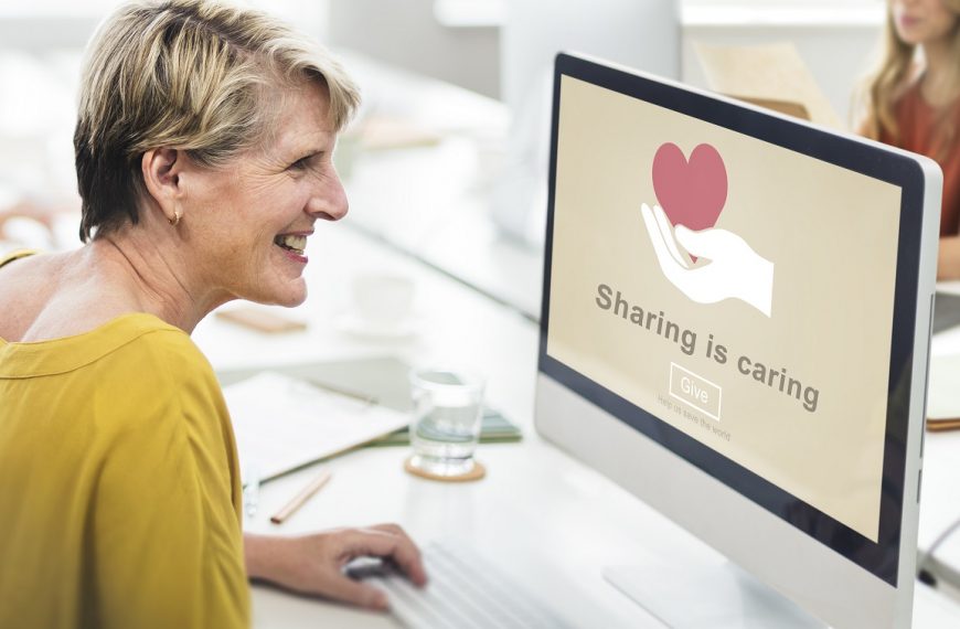 woman smiling while looking at a monitor with the phrase 'sharing is caring' on the screen